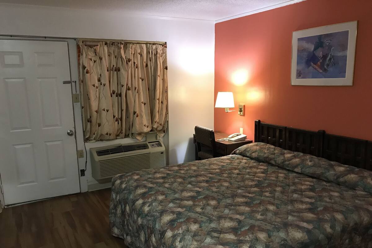 Una habitación de hotel con cama, escritorio con lámpara, teléfono y ventana con cortinas.