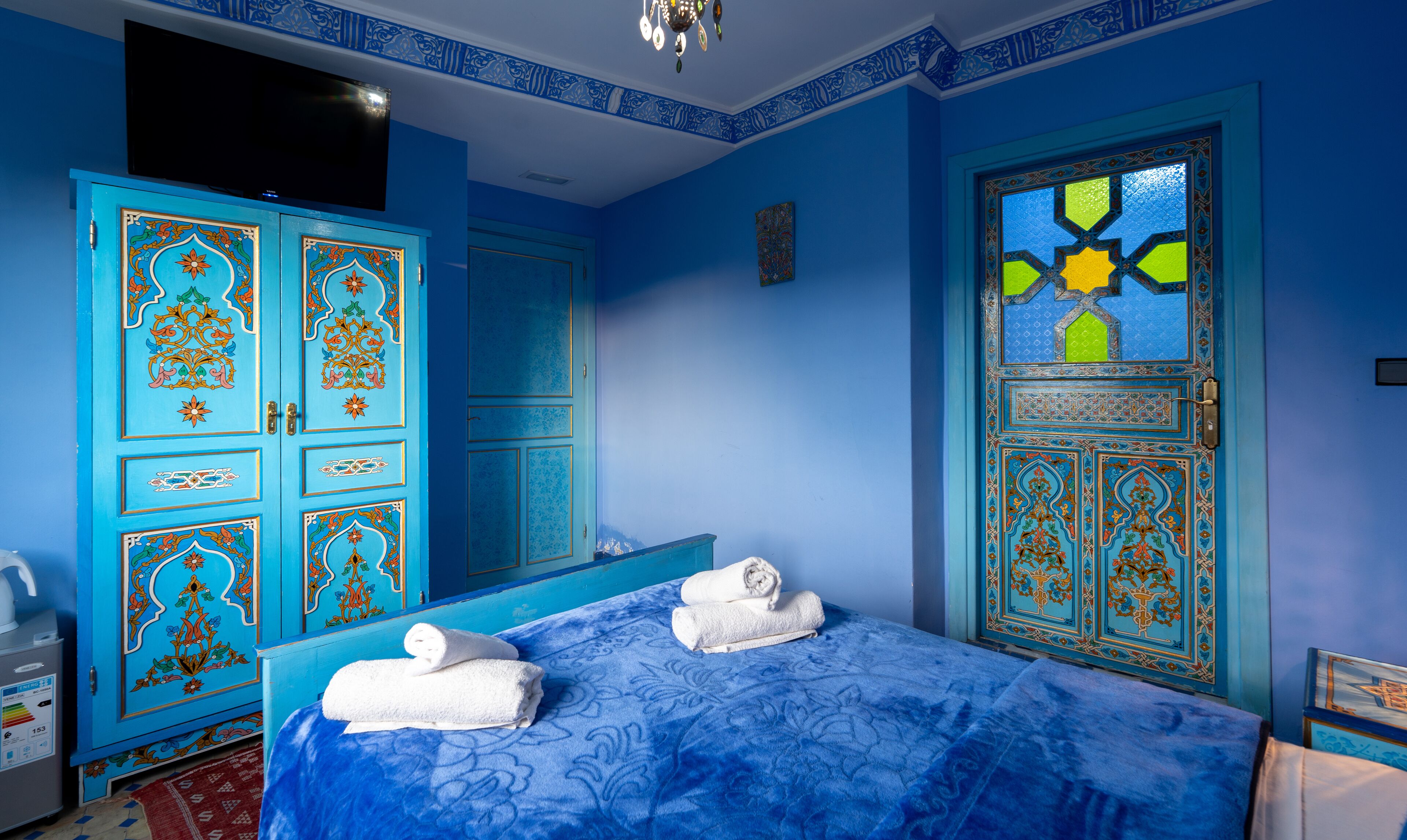 Une pièce comprenant un lit, une armoire bleue et une porte ornée de motifs complexes.