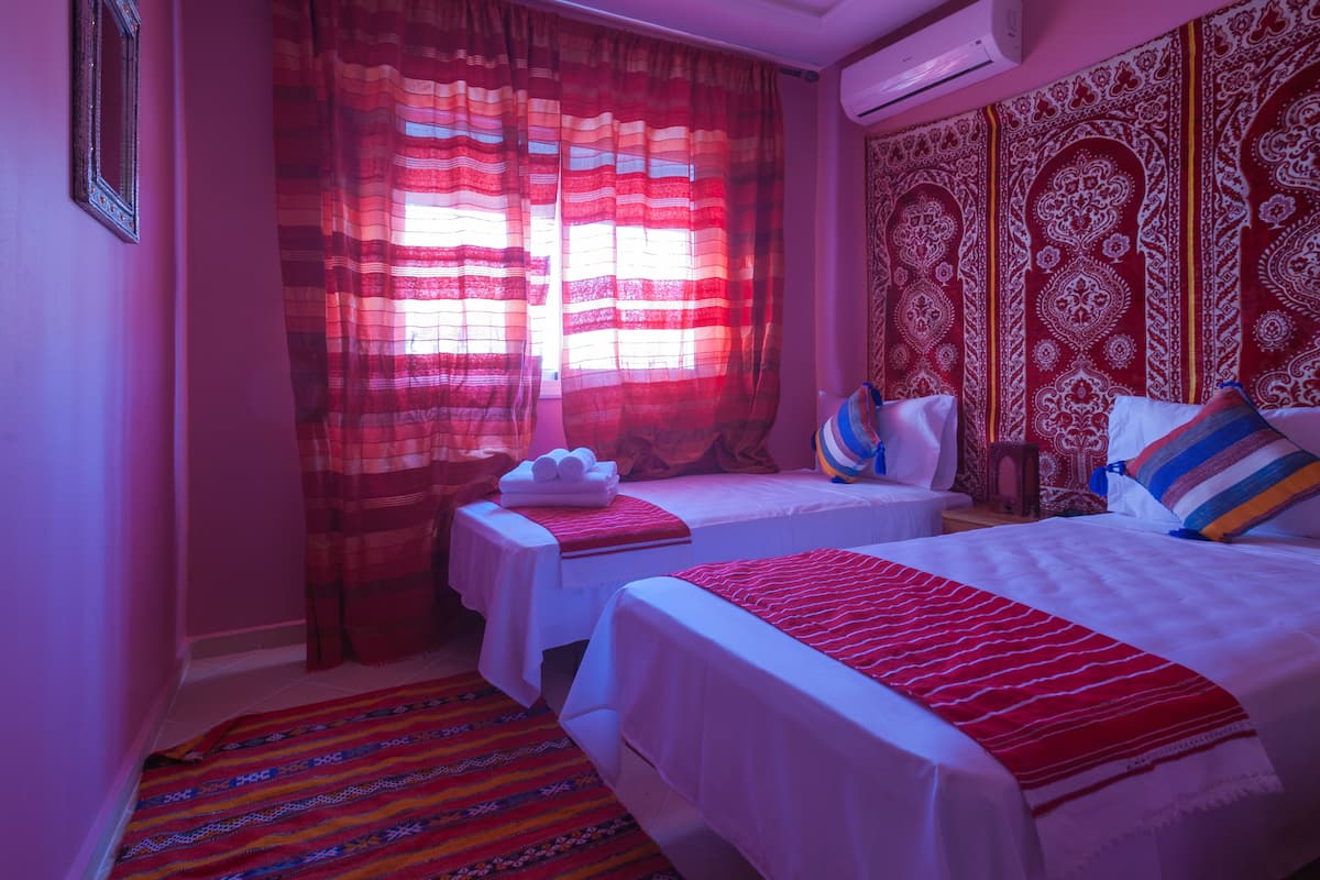 Habitación de hotel con dos camas, una cortina y un tapiz de pared, ambos con estampado rojo y blanco.