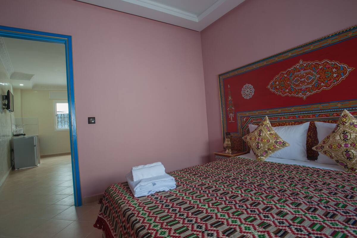 Una habitación de hotel con cama, mesita de noche, espejo y puerta que da a un baño.