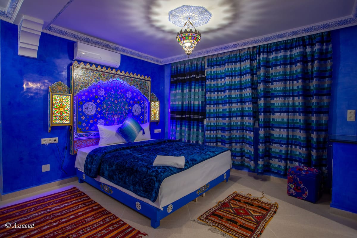 Un dormitorio con una cama grande, cortinas estampadas, una araña y un tapiz decorativo.