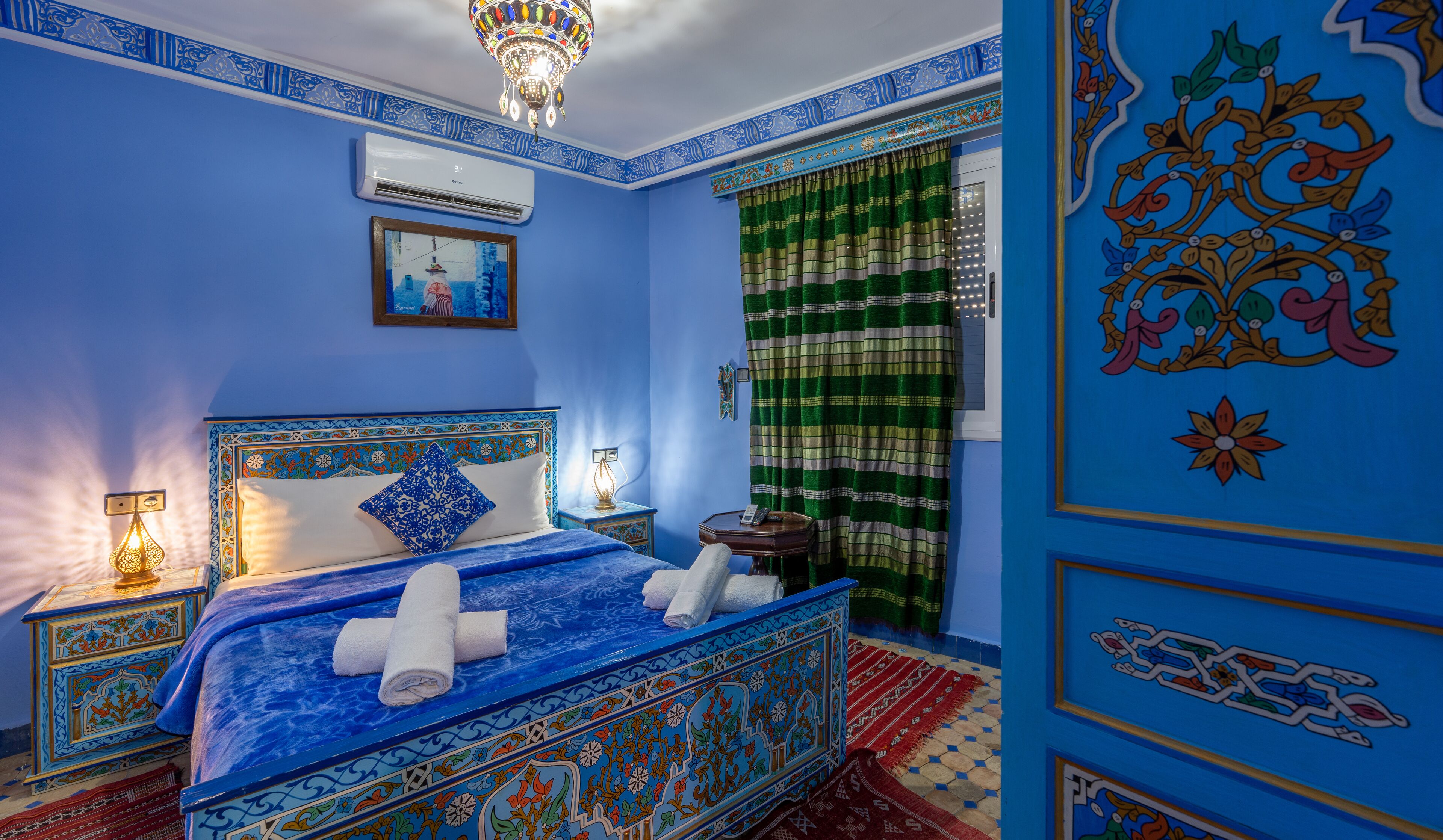 A room with a bed, a nightstand, a lamp, and a window with curtains.
