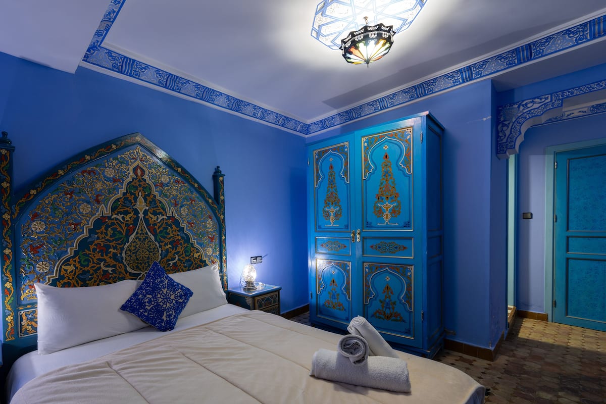 Una habitación con una cama grande, una mesita de noche, un armario azul y una puerta.