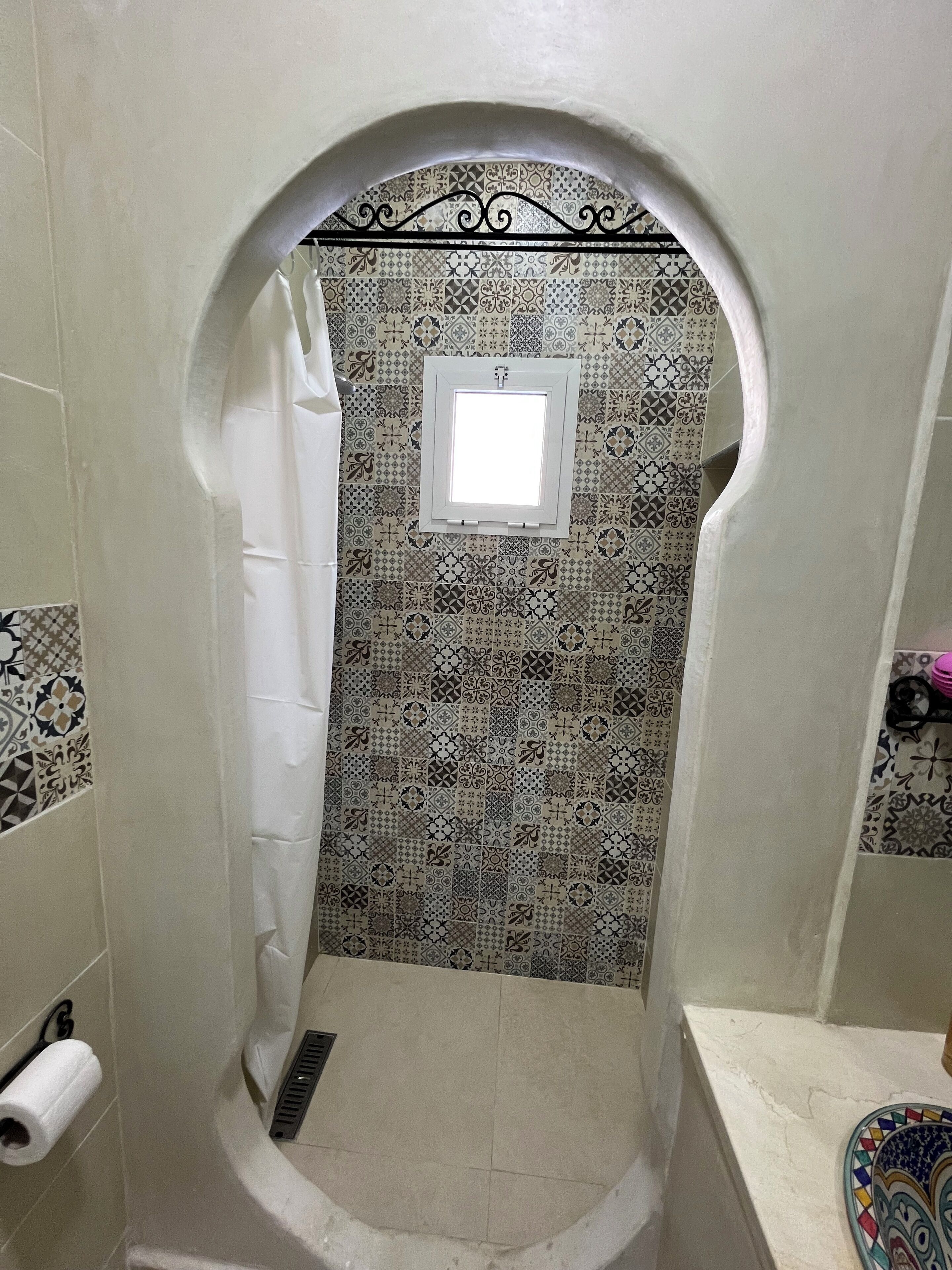 Un baño con zona de ducha azulejada, una ventana y un inodoro.