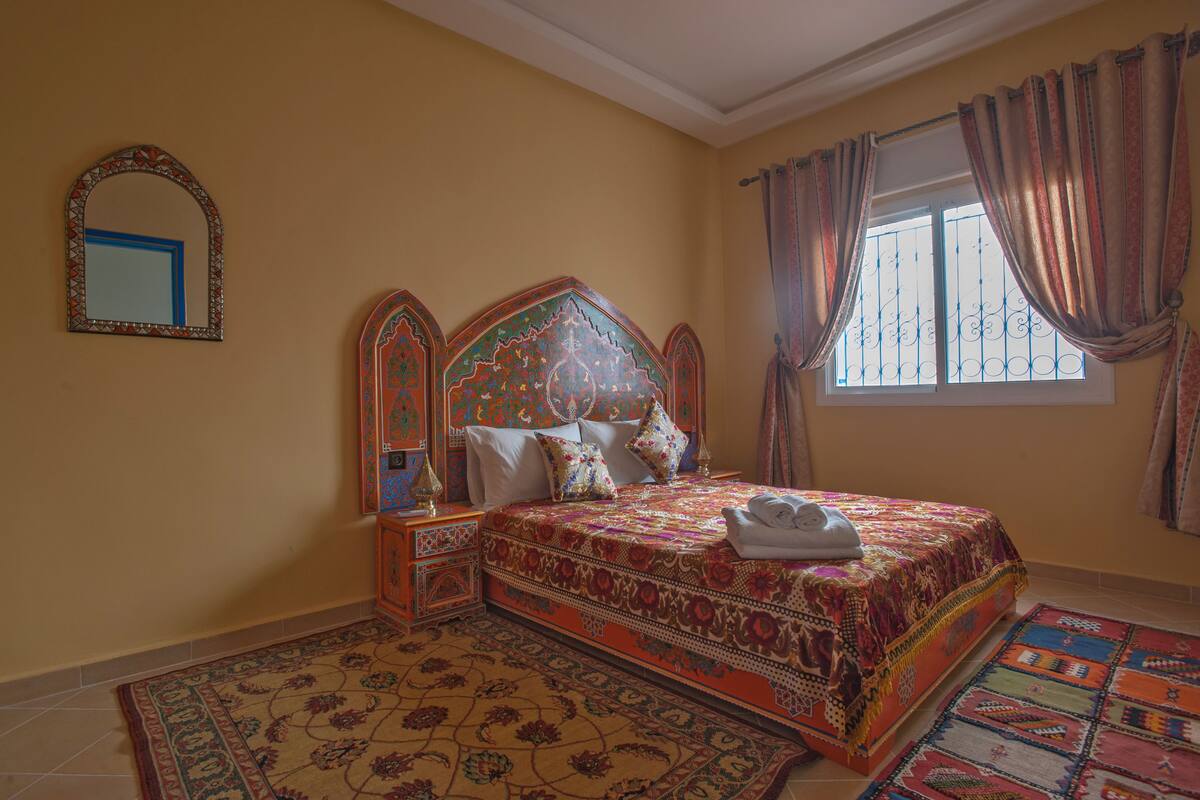 Un dormitorio con una cama grande, un cabecero ornamentado, un espejo y una ventana con cortinas.