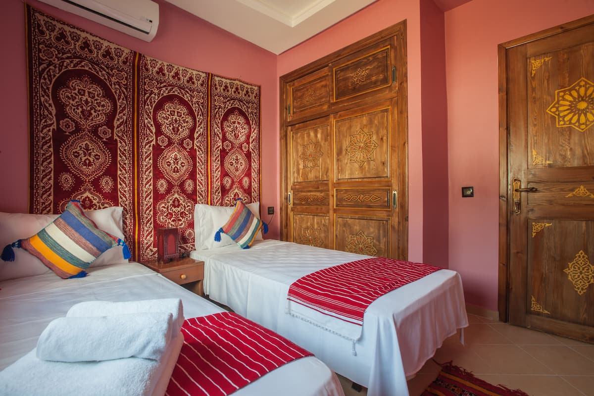 Habitación de hotel con dos camas, una puerta de madera grande y ornamentada, y un cabecero decorativo.