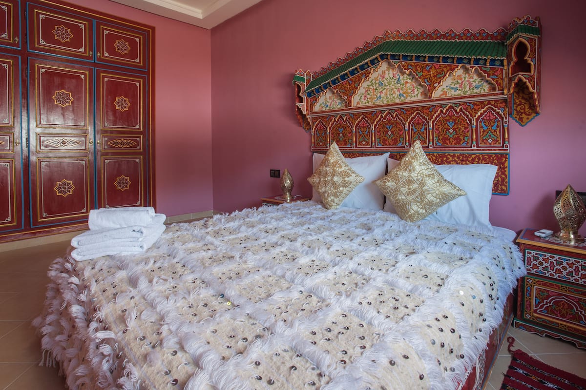 Una cama con una colcha blanca y esponjosa, un cabecero decorativo y una pared roja con una puerta de madera.