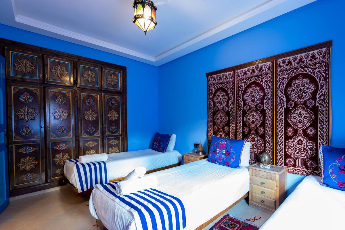 Una habitación con dos camas, una mesita de noche y un armario con detalles ornamentales.