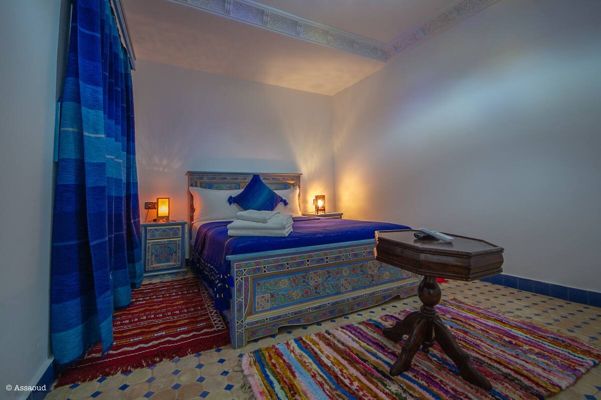 Un dormitorio con una cama, mesitas de noche, una mesilla auxiliar y una alfombra estampada.