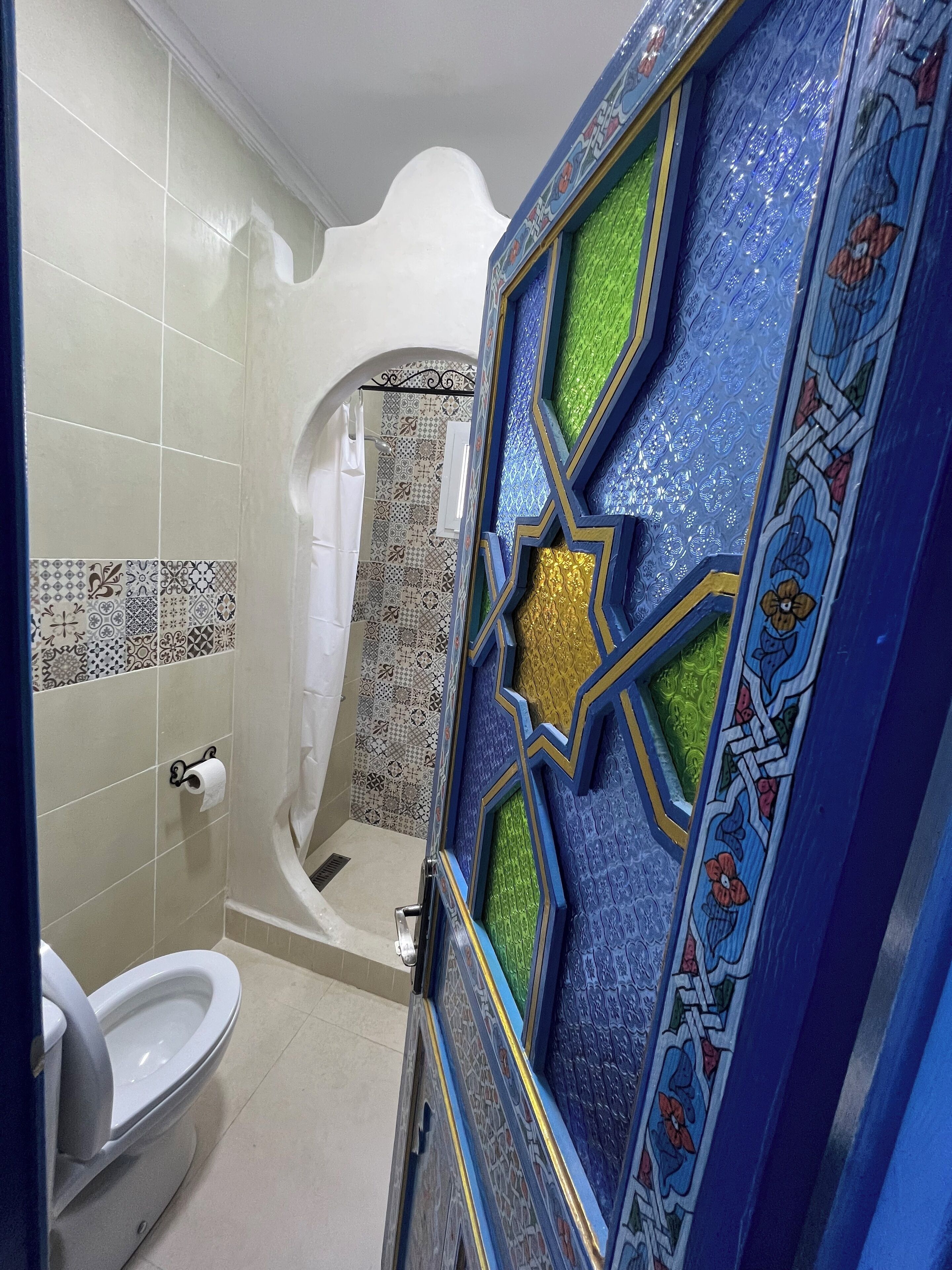 Un bany amb vàter, dutxa i una porta decorativa amb motius geomètrics.