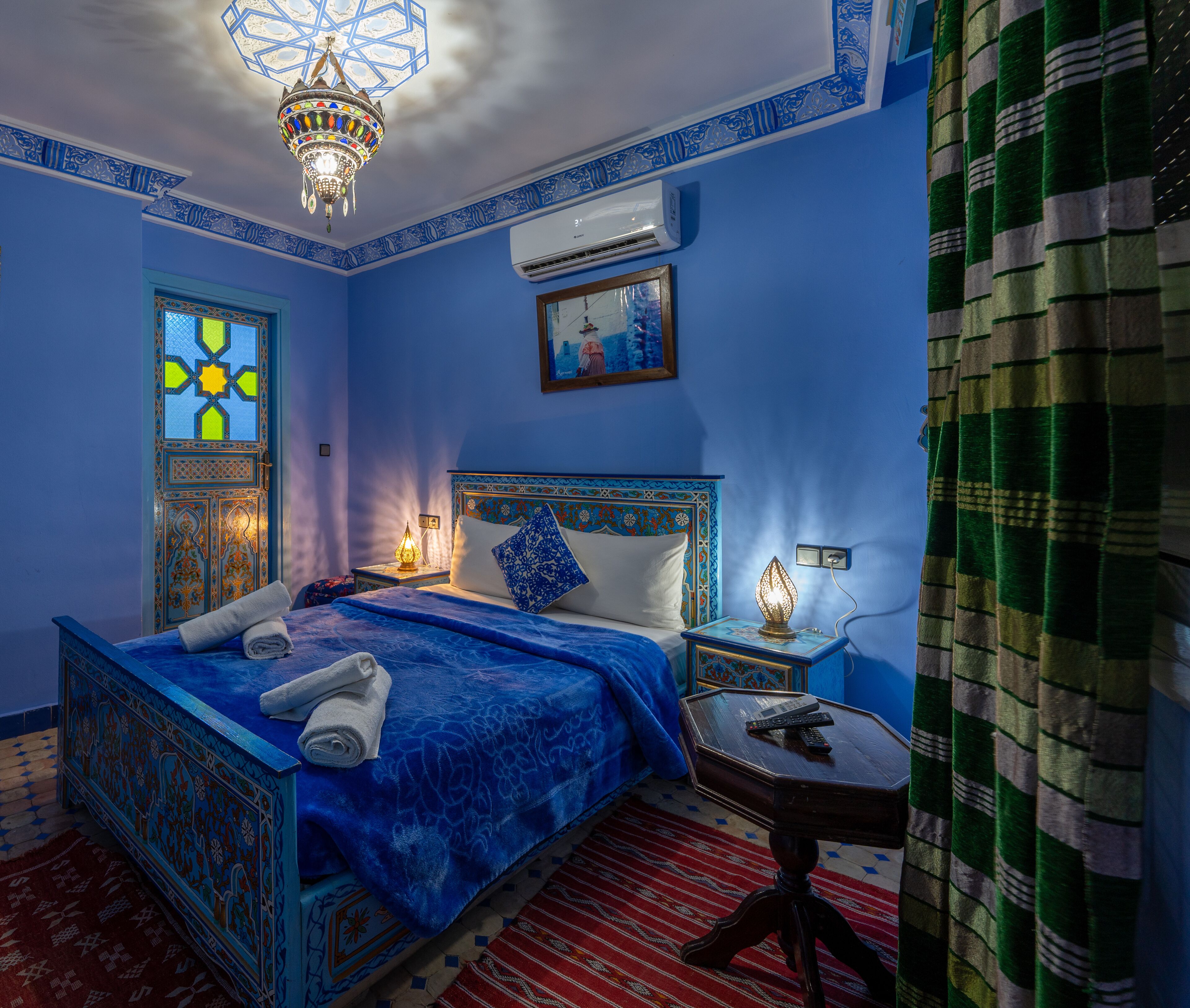 Una habitación con cama, mesita de noche, aire acondicionado de pared y una lámpara decorativa.