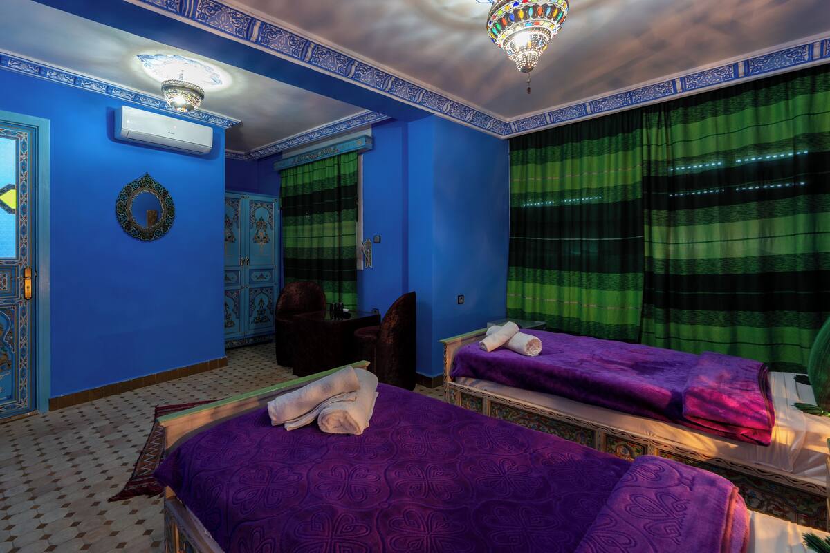 Una habitación con dos camas, una araña y un papel tapiz azul y verde estampado.