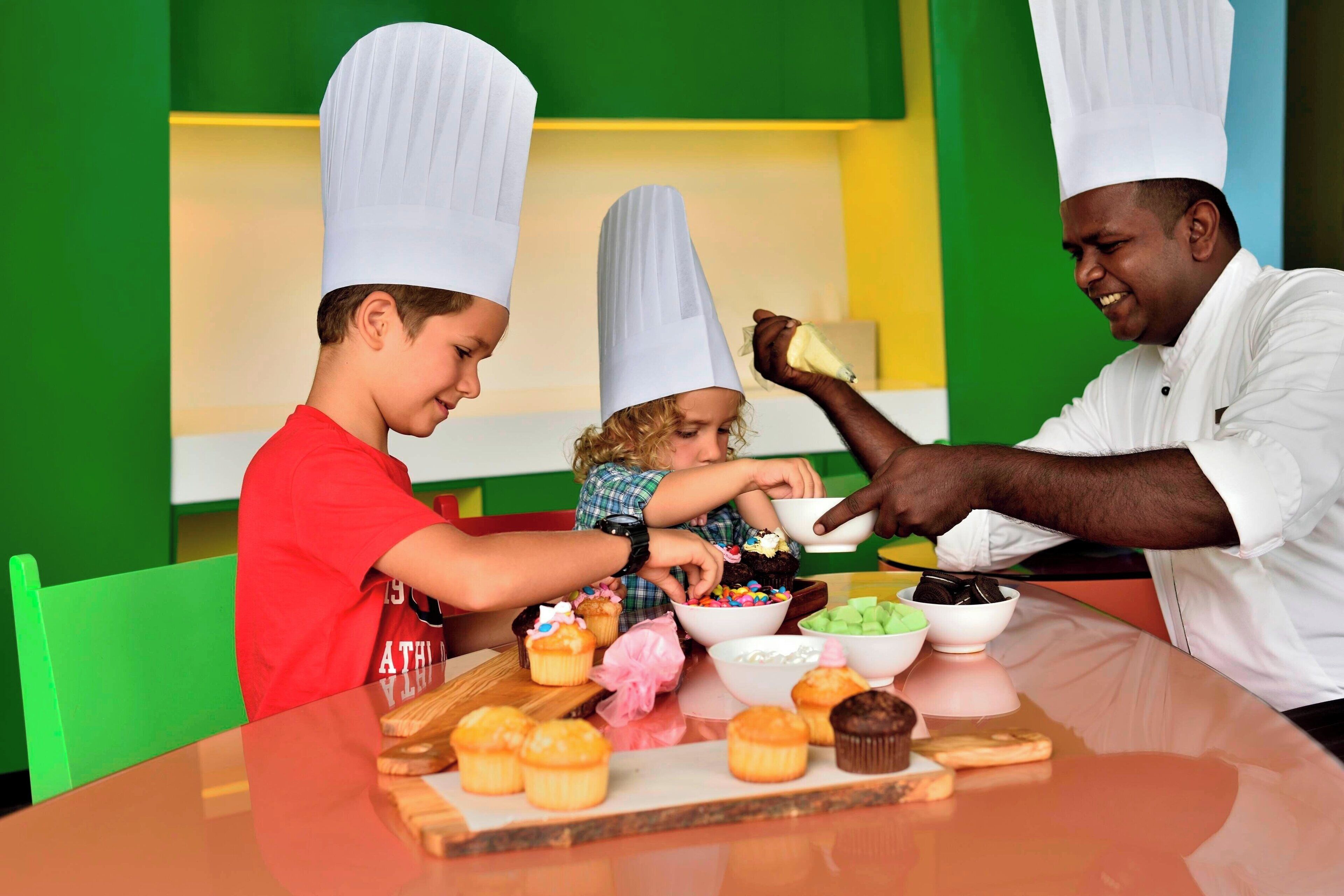A group of people wearing chef hats, seated at a table with various food items and bowls.