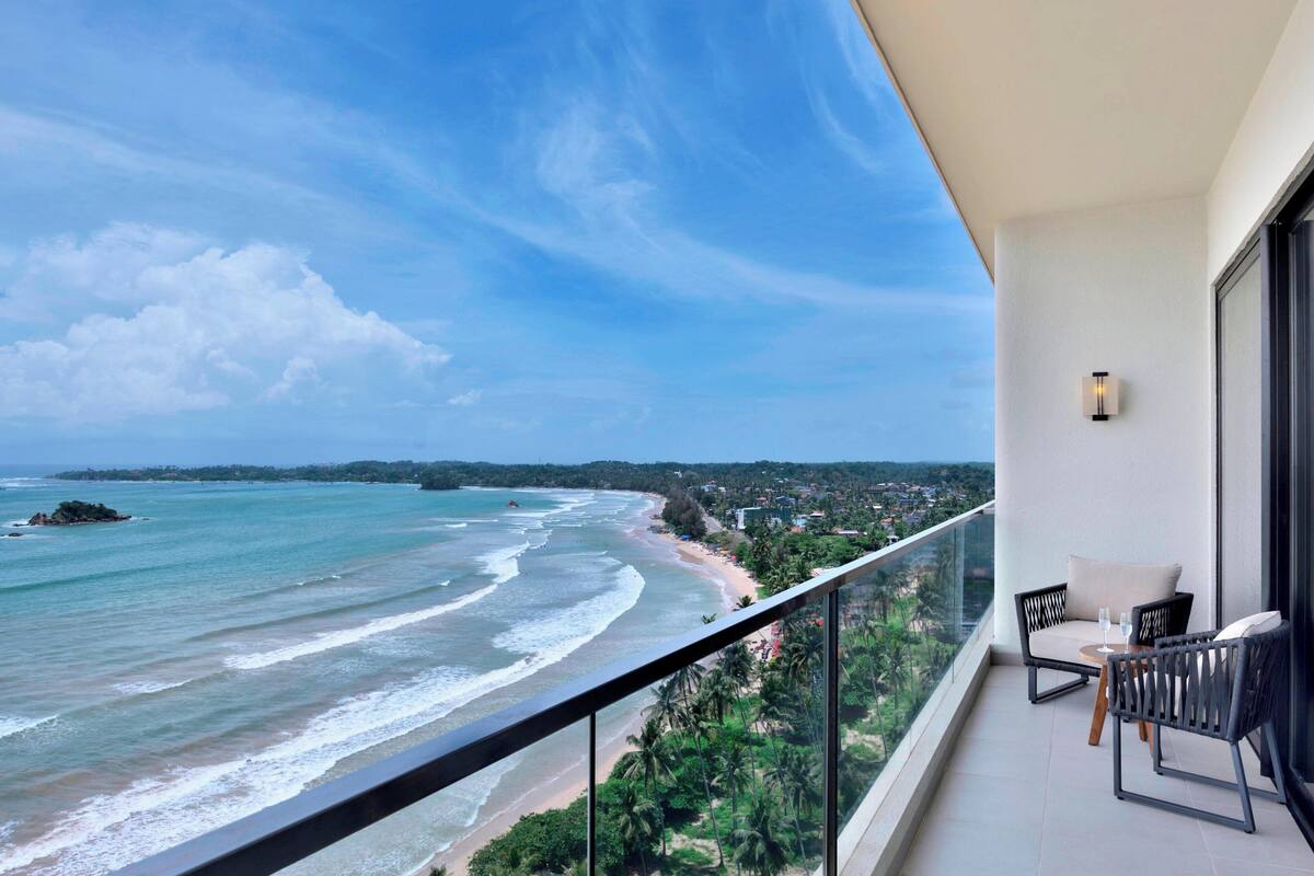 Ein Balkon mit Blick auf den Ozean und den Strand, ausgestattet mit Stühlen und einem Tisch.