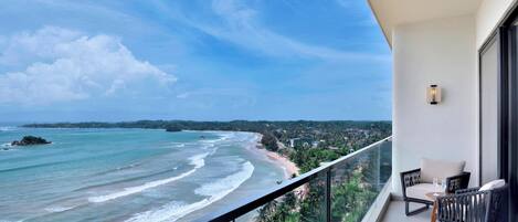 A balcony with a view of the ocean and beach, furnished with chairs and a table.