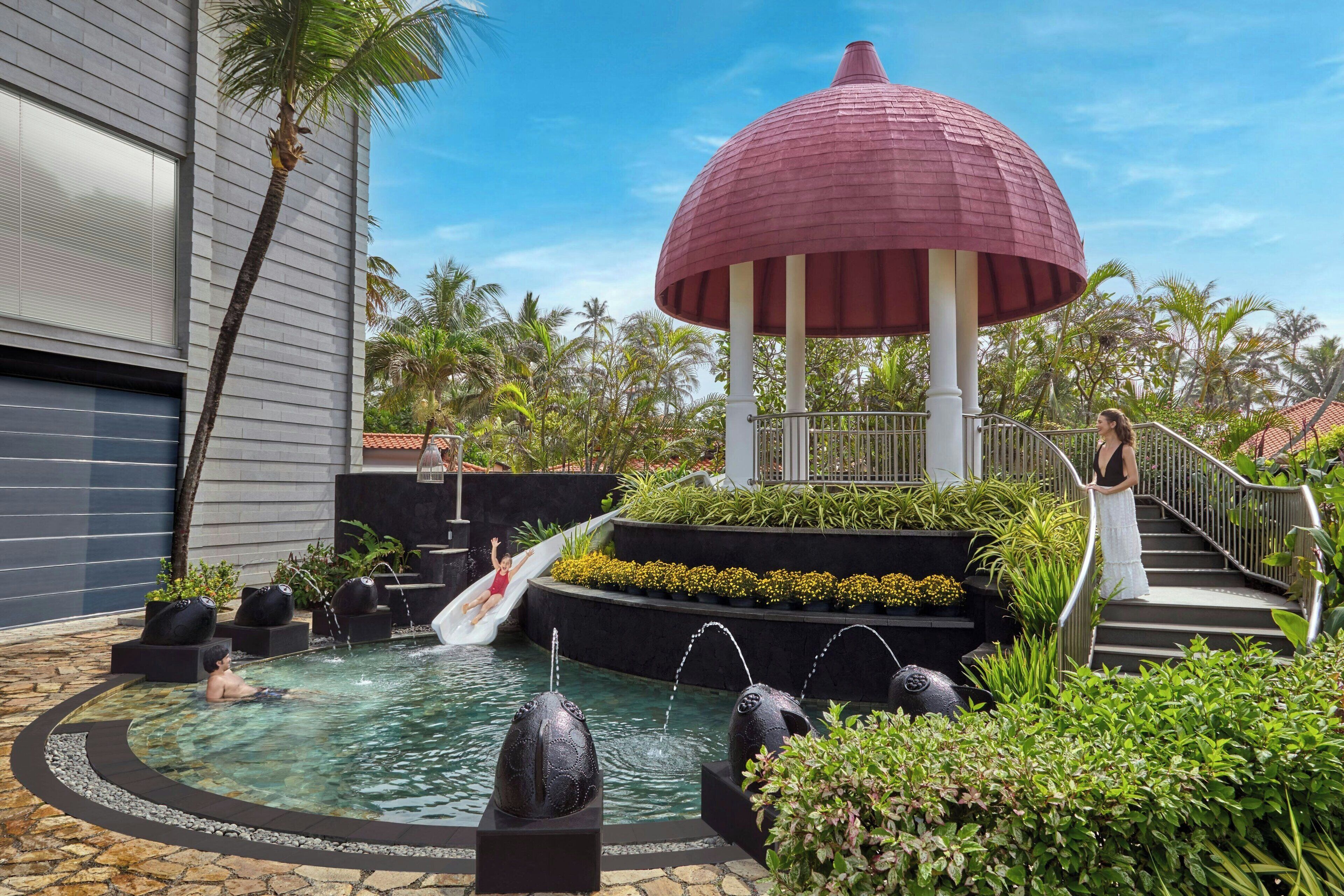 A pool area with a slide, a red umbrella structure, and a staircase leading to a covered area.