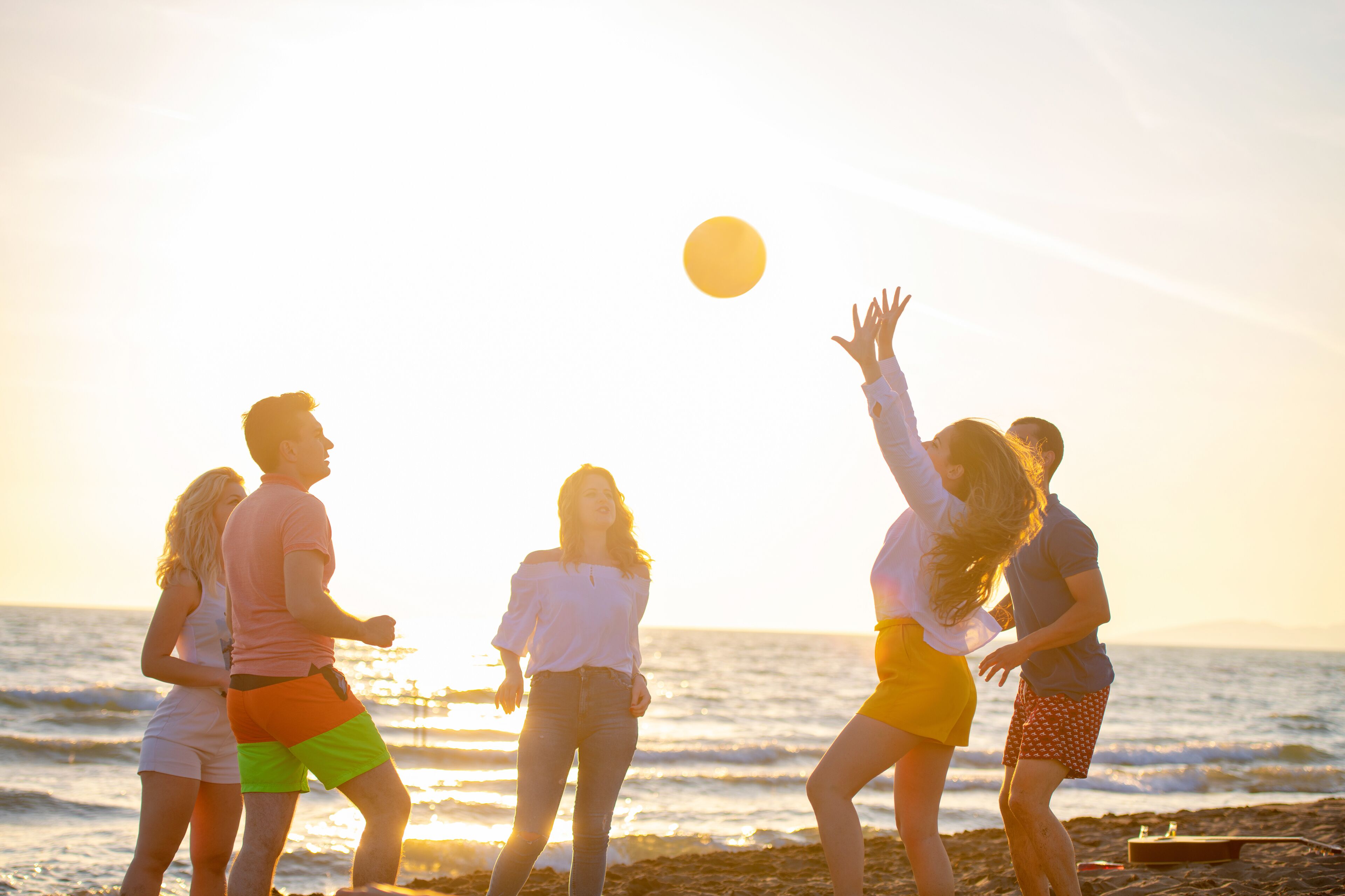 A group of people playing with a ball on a beach during sunset.