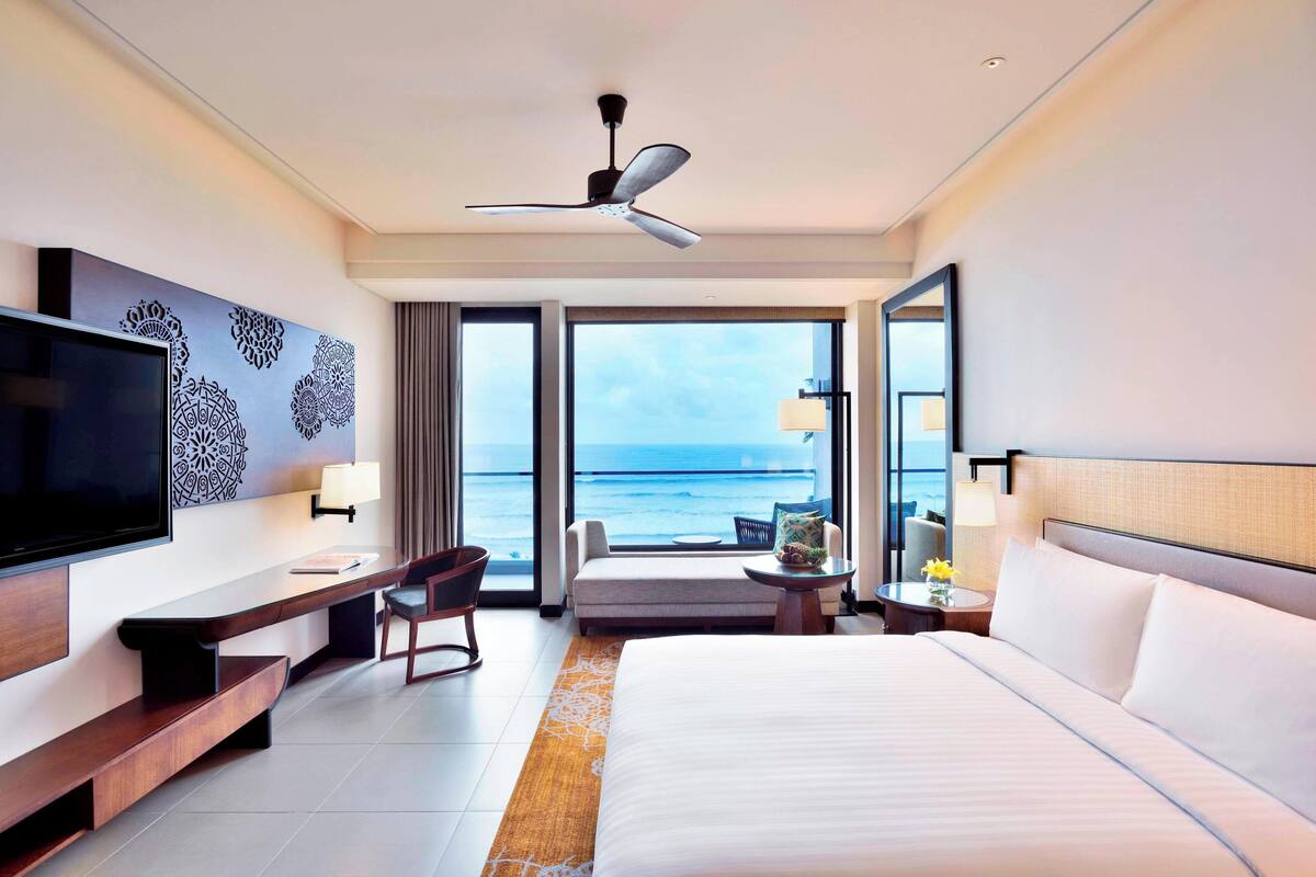 Ein Hotelzimmer mit einem großen Bett, einem Schreibtisch, einem Fernseher, einem Deckenventilator und Blick aufs Meer.