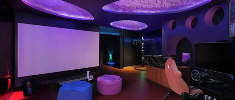 Una habitación moderna con una pantalla grande, una silla gamer y luces circulares en el techo.