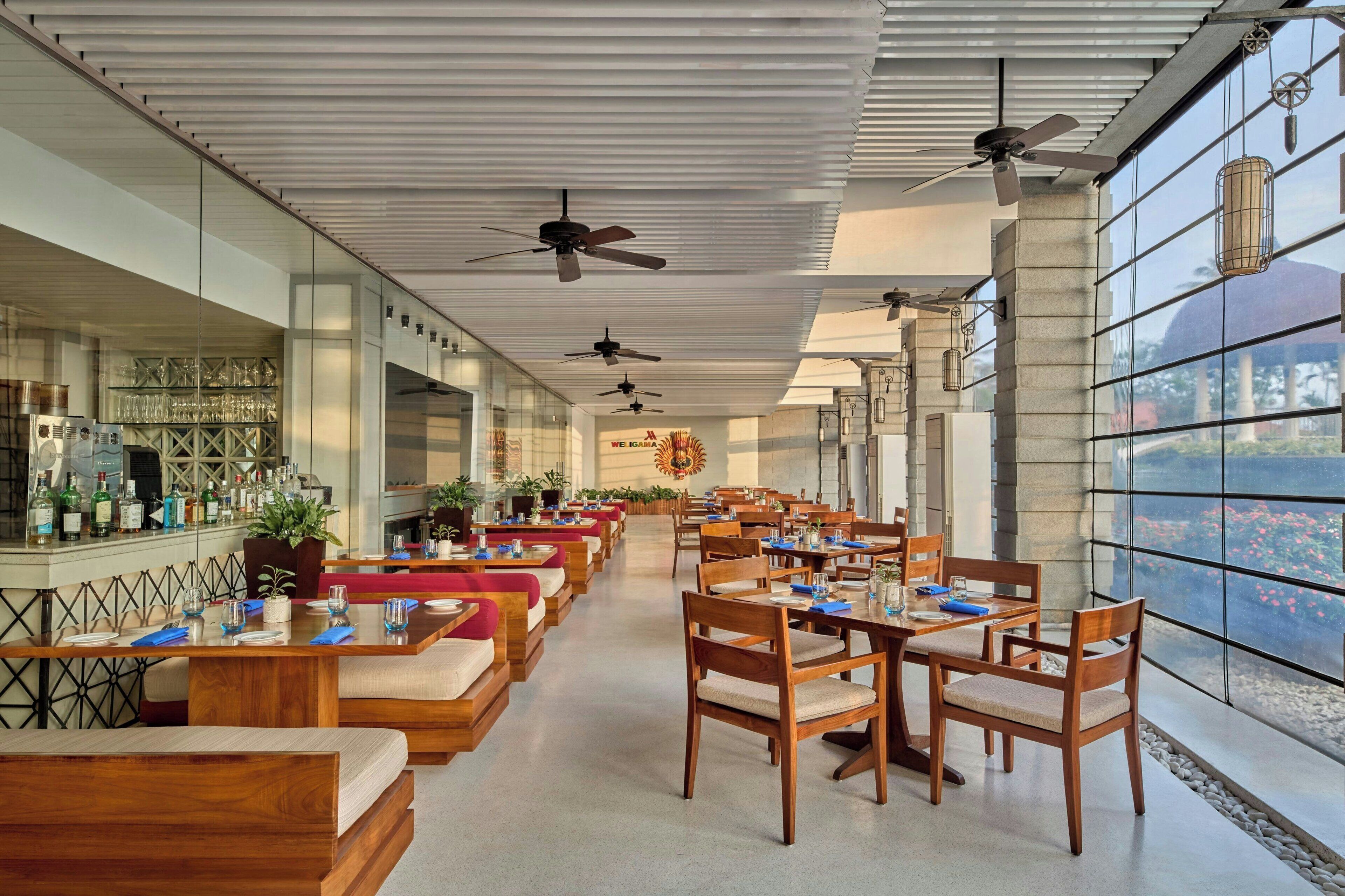 Ein geräumiges Restaurant mit hohen Decken, Deckenventilatoren und großen Fenstern mit Blick ins Freie.
