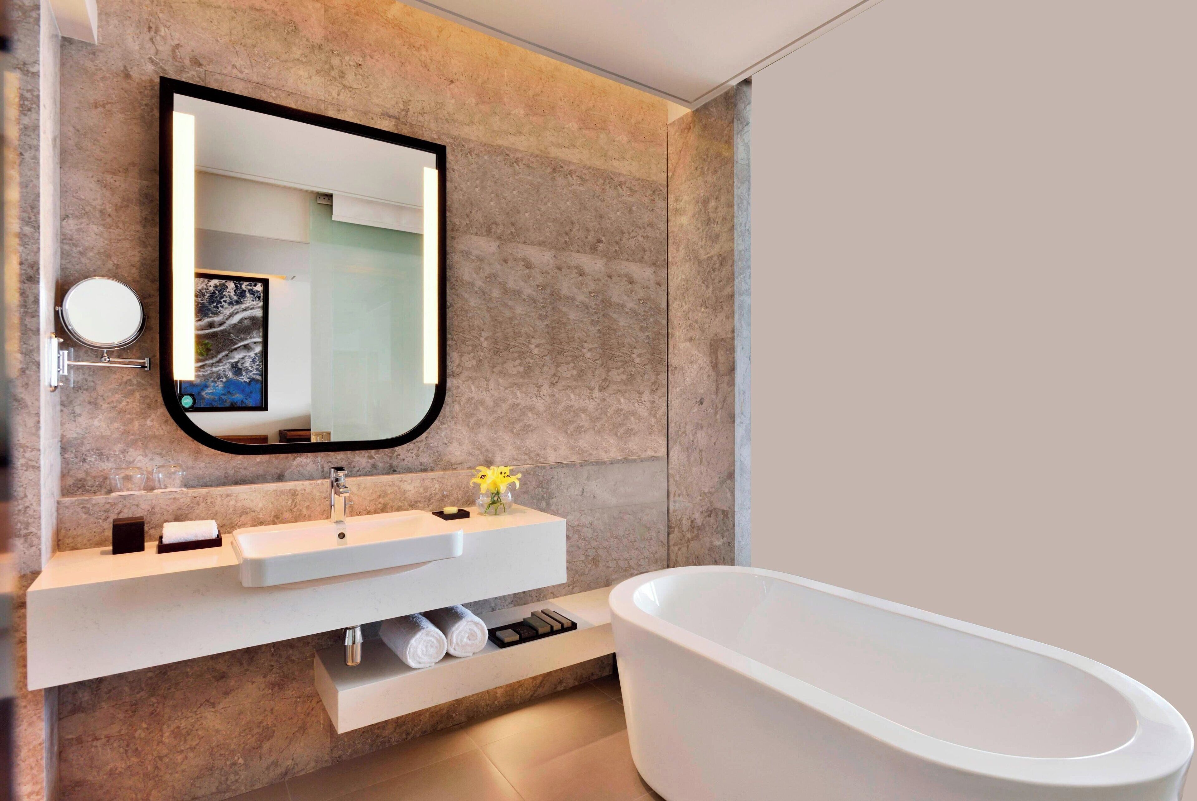 A modern bathroom with a freestanding bathtub, a large mirror, and a marble wall.