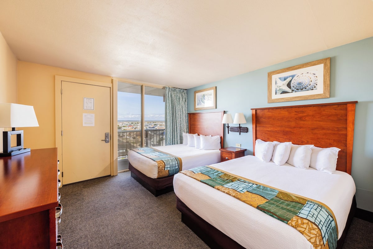 A hotel room with two beds, a desk, a chair, a nightstand, and a view of the city.