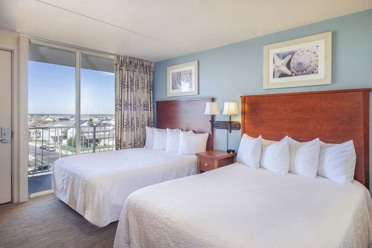 A hotel room with two beds, a large window with a view, a wooden headboard, and a framed picture on the wall.