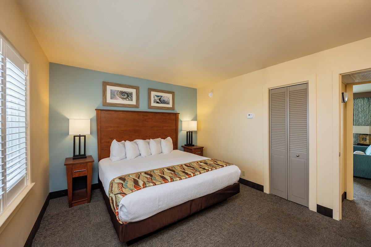 A hotel room with a large bed, two bedside tables with lamps, a wooden headboard, and a door with a mirror.