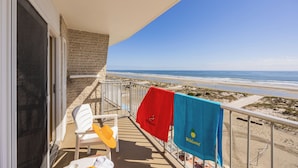 A balcony with a view of the beach, a white chair, and two towels hanging on the railing. - Reges Oceanfront Resort (Wildwood Crest)