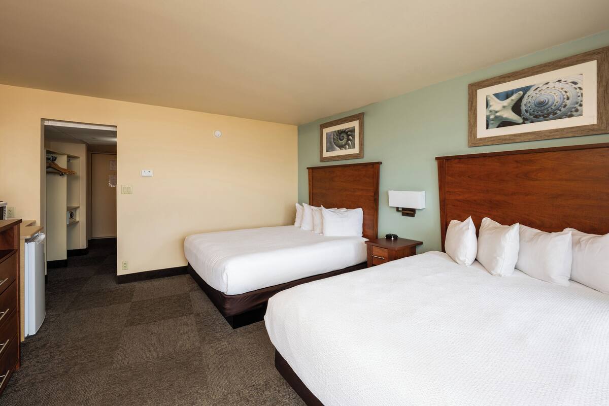 A hotel room with two beds, a wooden headboard, a framed picture on the wall, and a small bedside table with a lamp.
