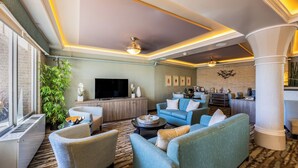 A modern living room with a large flat-screen TV, comfortable seating, a potted plant, and a patterned carpet. - Reges Oceanfront Resort (Wildwood Crest)