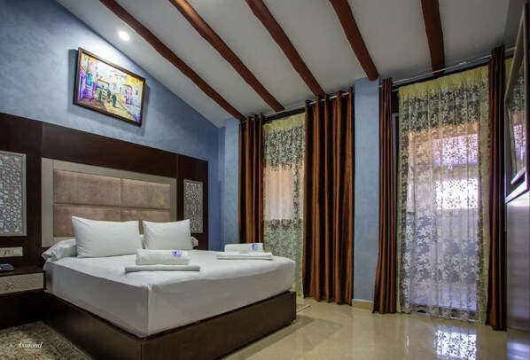 Una habitación de hotel con una cama grande, un cabecero, un cuadro en la pared y cortinas en las ventanas.