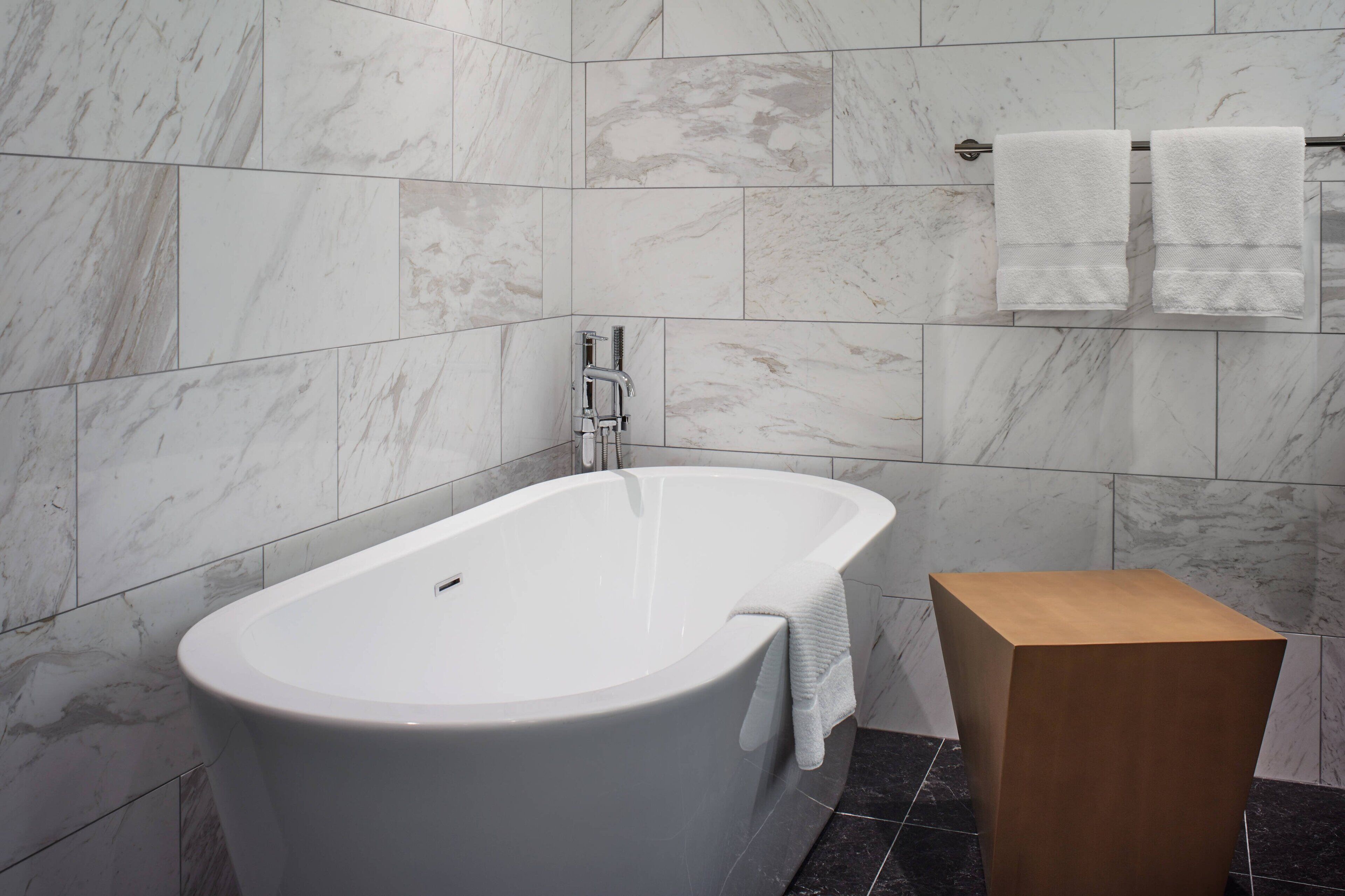 Une salle de bain moderne avec une baignoire sur pieds, des carreaux de marbre et une petite table d’appoint en bois.