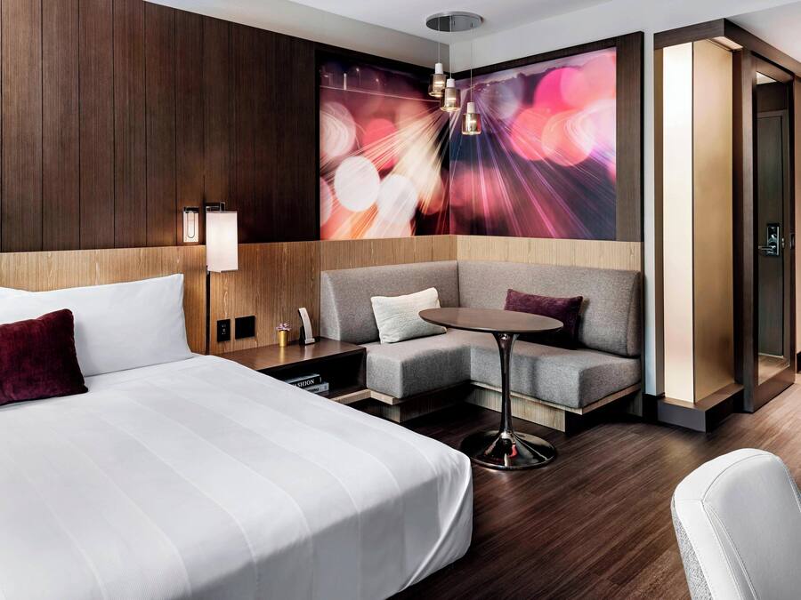 Ein modernes Hotelzimmer mit einem großen Bett, einer Sitzecke, einem kleinen Tisch und einem Wandgemälde.