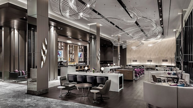 Un moderno vestíbulo de hotel con un bar central, zonas de estar y un diseño de techo único.
