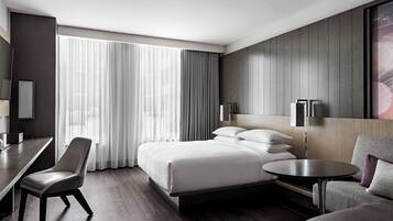 A modern hotel room with a large bed, a desk, a chair, and a small table.
