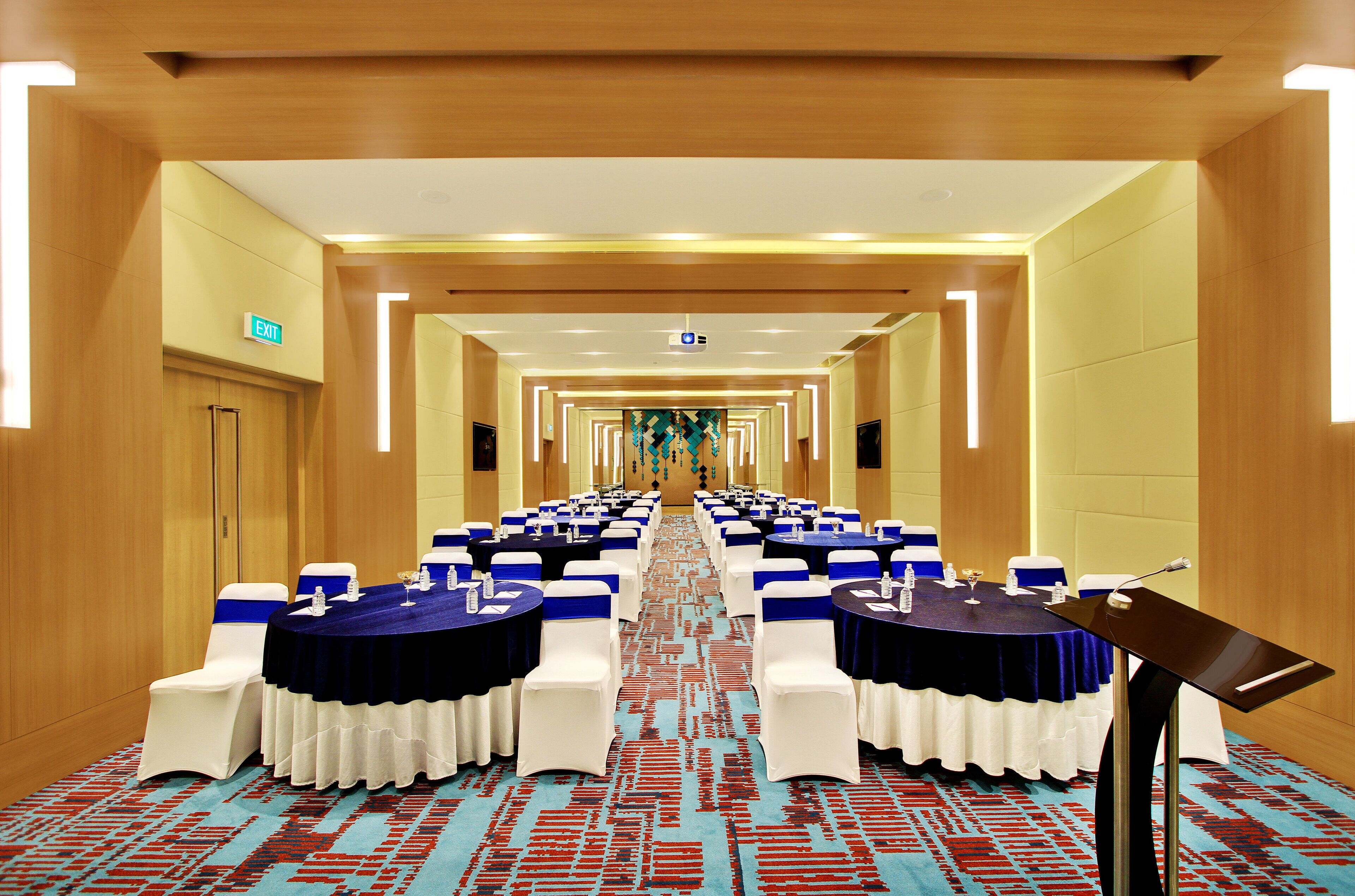 A conference room with rows of tables and chairs, a podium, and an exit sign.