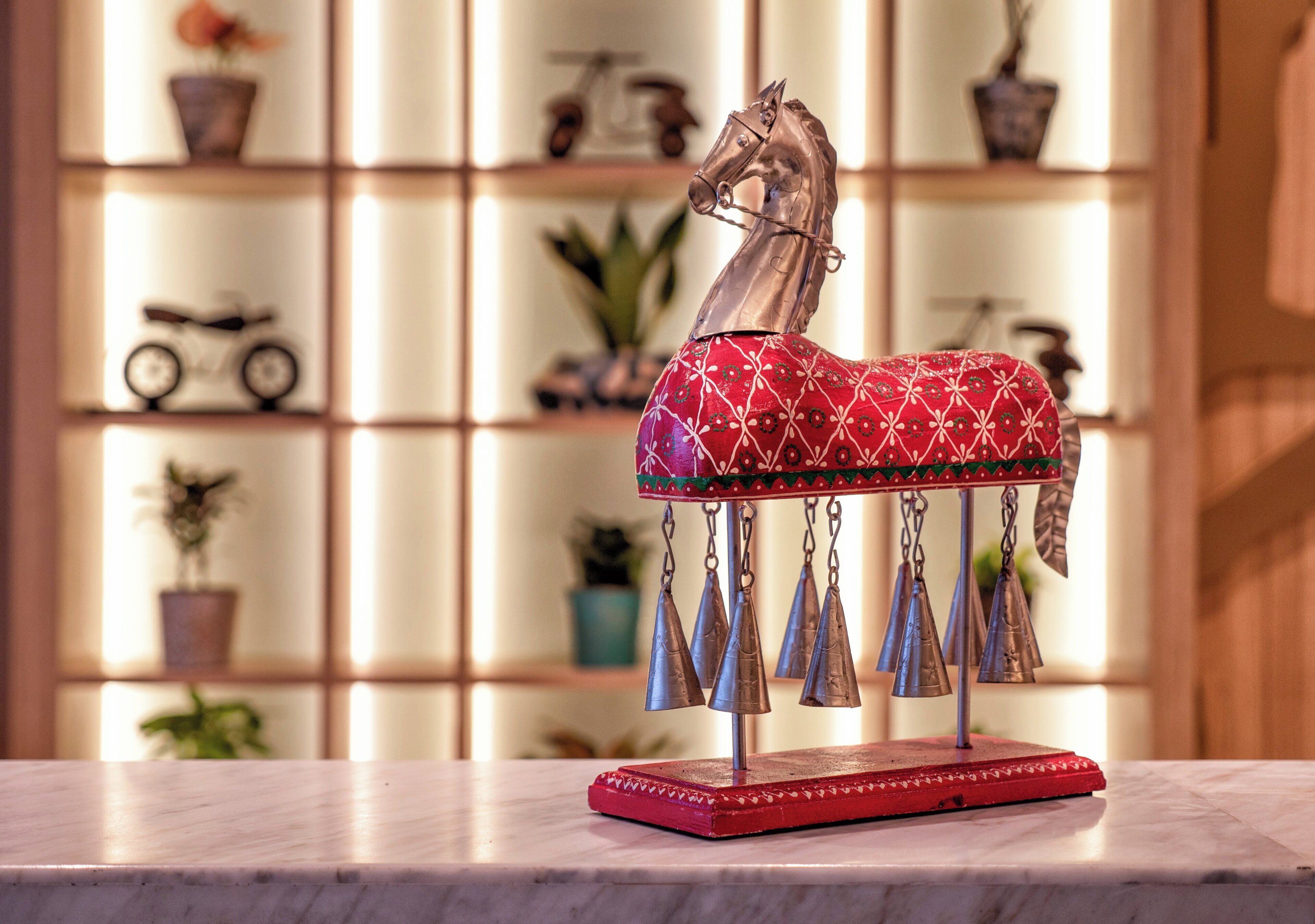 A decorative horse sculpture with a red and white patterned saddle and blue tassels on a marble surface.