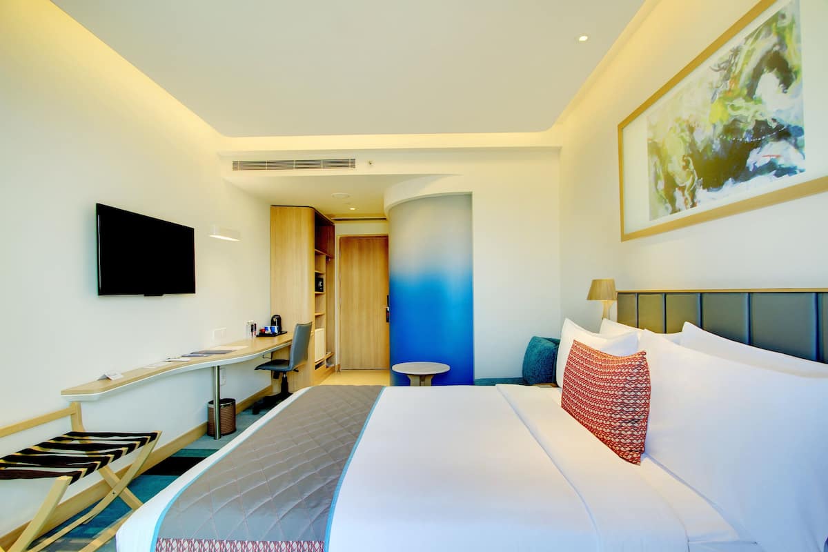 A modern hotel room with a large bed, a flat-screen TV, a desk with a chair, and a small table.