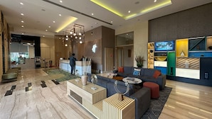 Un moderno vestíbulo de hotel con una recepción, zona de estar y un televisor montado en la pared.