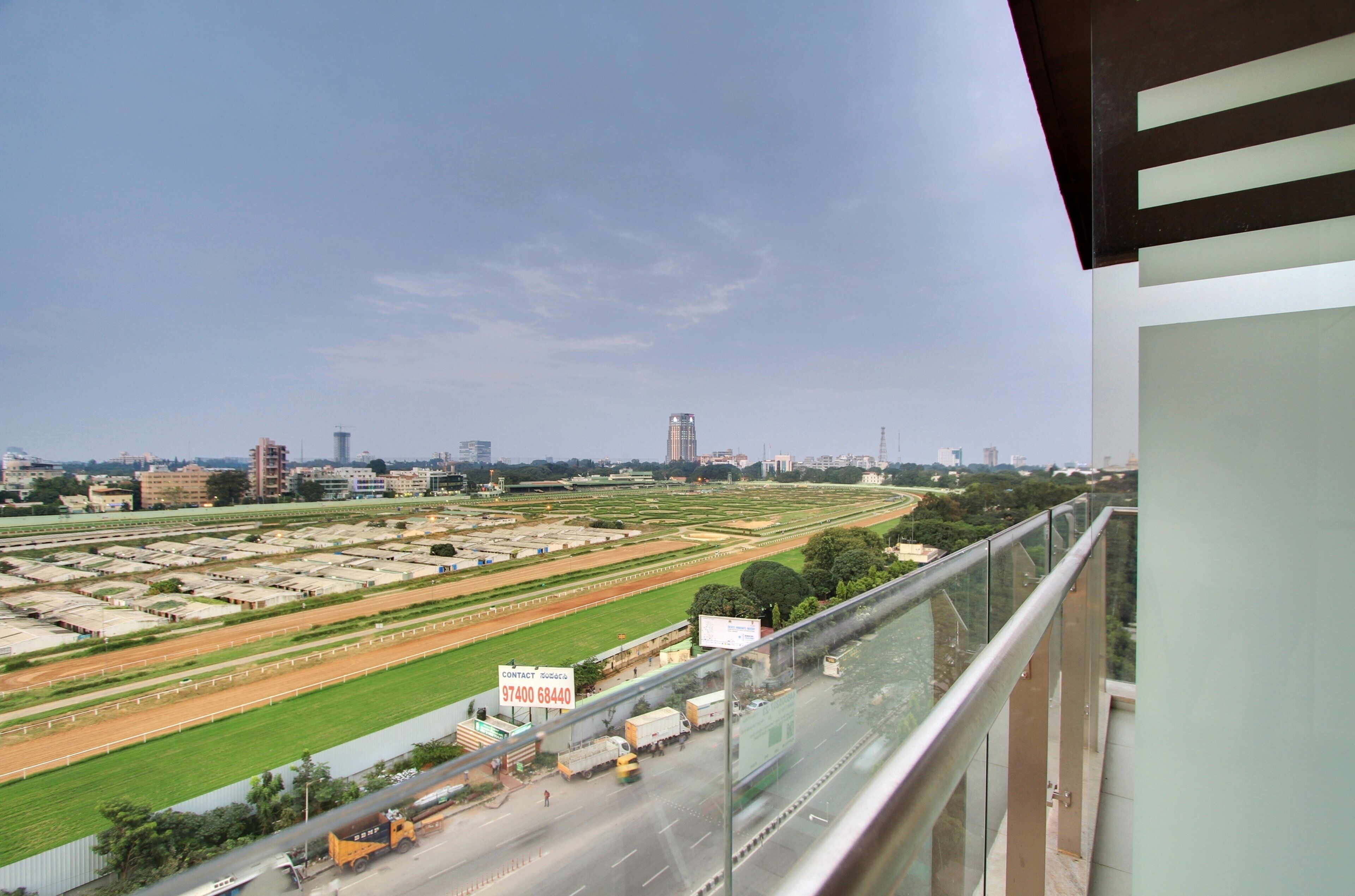 Vista desde un balcón sobre un gran complejo deportivo con varias pistas y campos, una carretera con vehículos y edificios al fondo.
