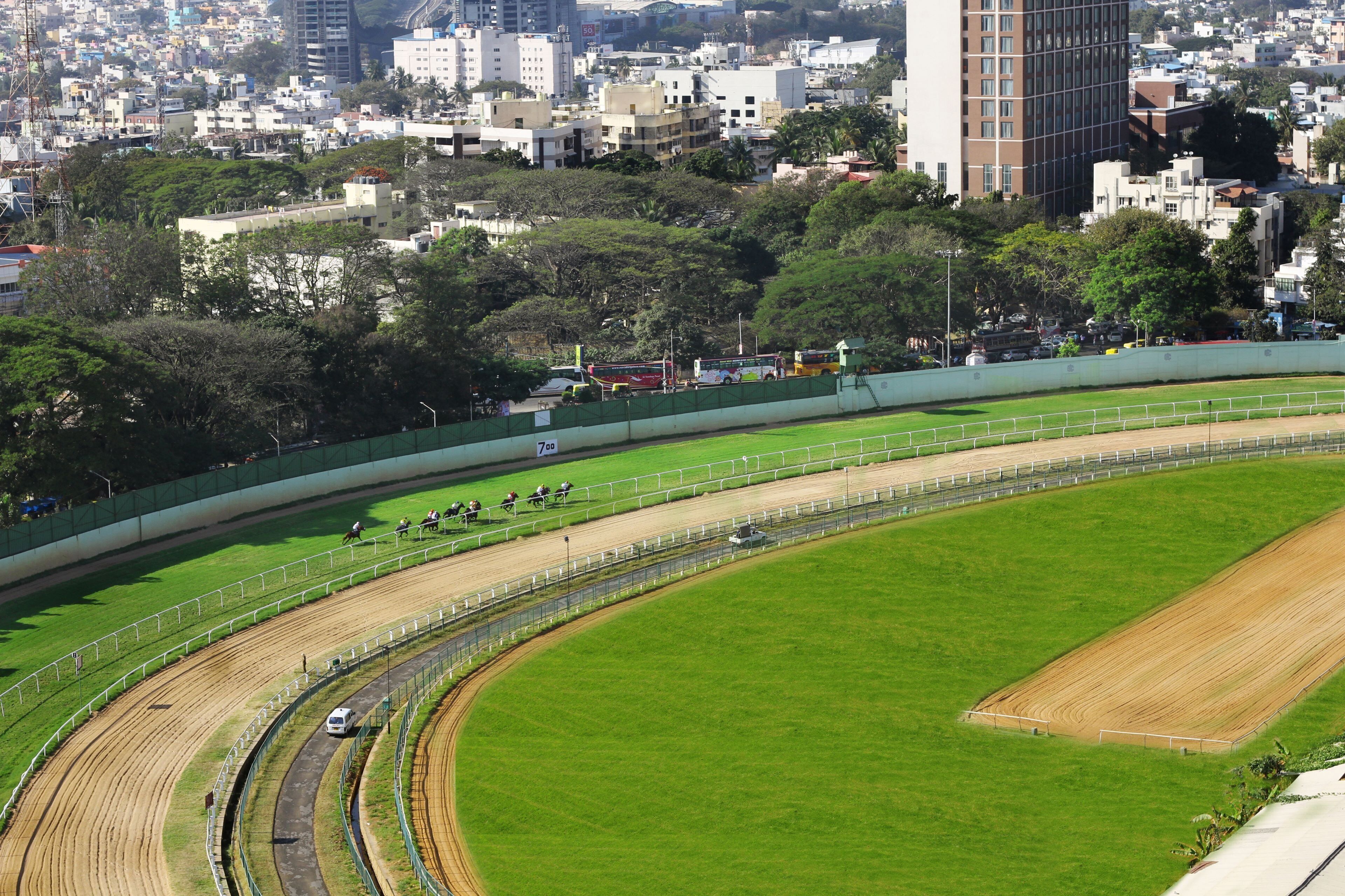 A racetrack with a green field, spectator stands, and a cityscape in the background.