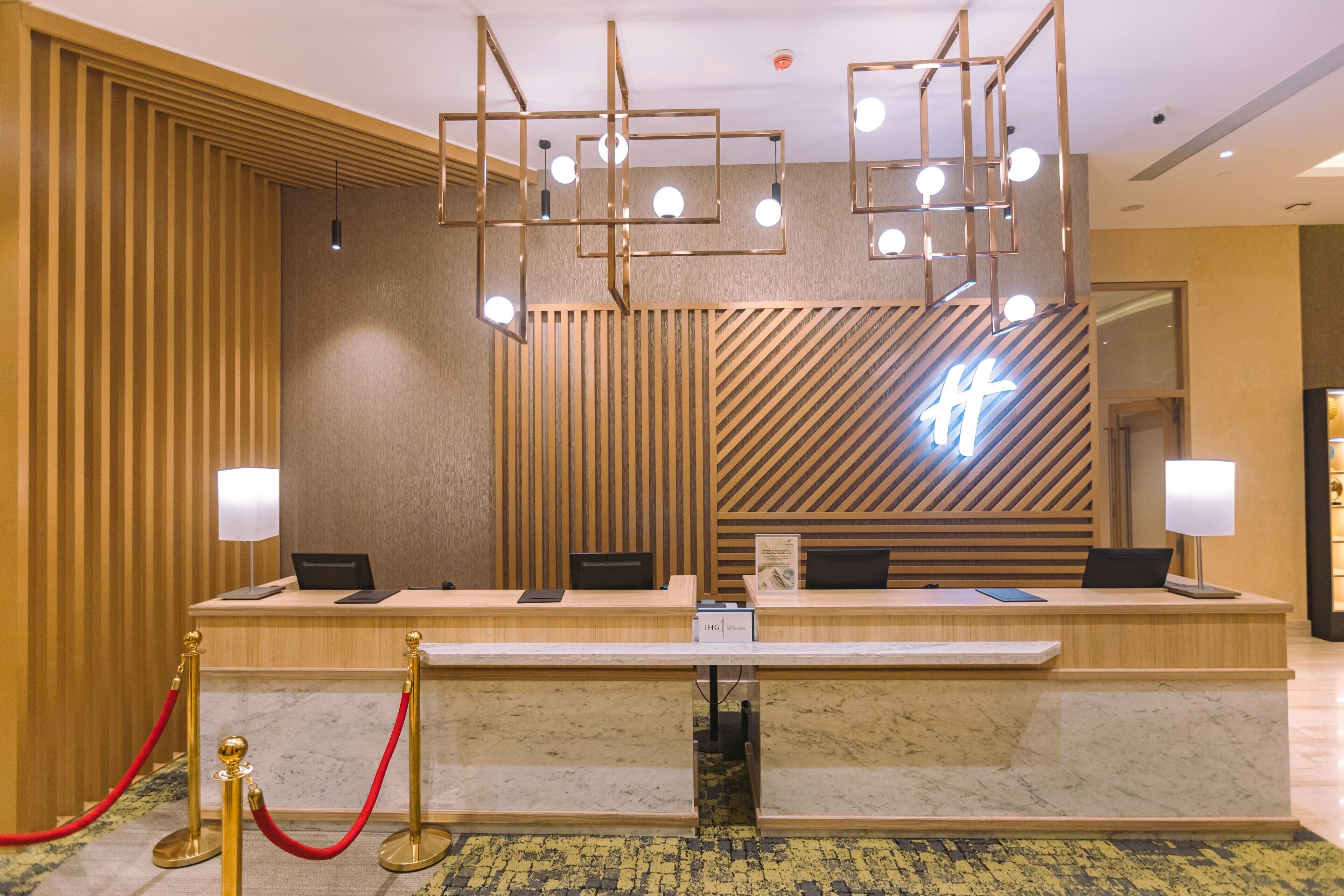 Un mostrador de recepción de hotel con diseño moderno, que incluye un panel de pared de madera, un letrero de neón y una encimera de mármol.