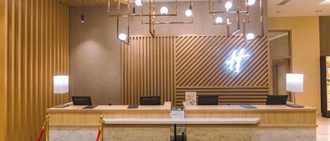 A hotel reception desk with a modern design, featuring a wooden panel wall, a neon sign, and a marble counter.