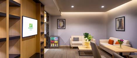 A modern hotel lobby with a reception desk, seating area, and a refrigerator stocked with beverages.