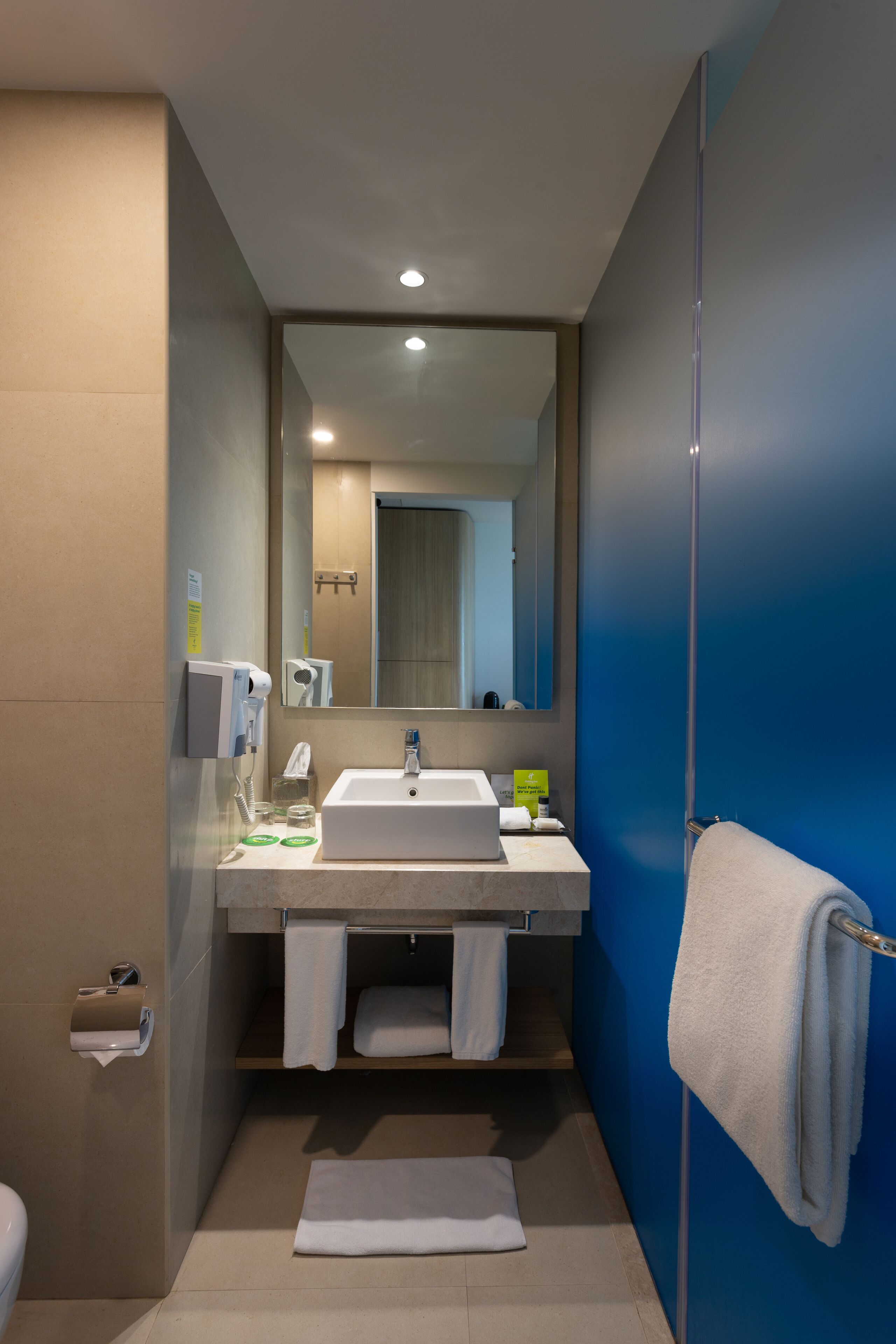 Un baño moderno con un lavabo blanco, un espejo, un perchero para toallas y una cabina de ducha con mampara de vidrio.