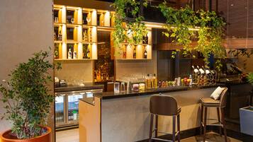 A bar area with a marble countertop, two bar stools, shelves with bottles and glasses, and a large potted plant.
