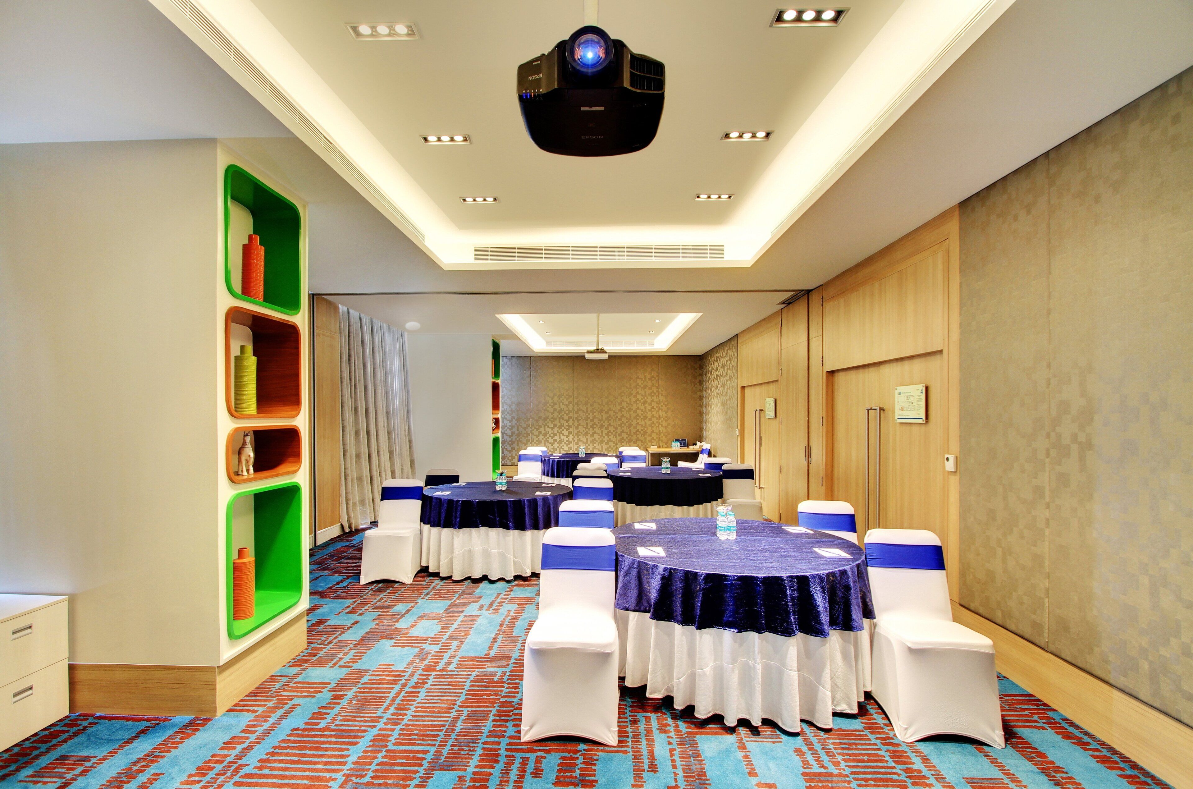 A conference room with round tables, white chairs, and a projector on the ceiling.
