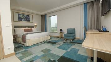 A hotel room with a bed, a desk, a chair, a TV, and a window with curtains.