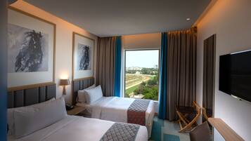 Habitación de hotel con dos camas, televisión, escritorio y vistas a un paisaje urbano.